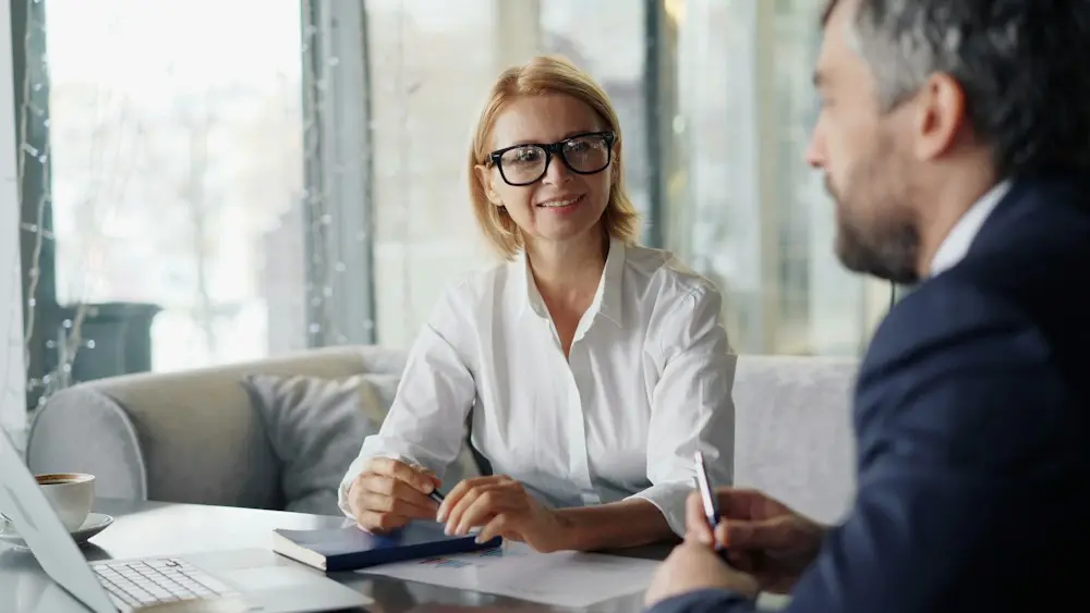 Consultor conversando com uma cliente sorridente diante de um notebook