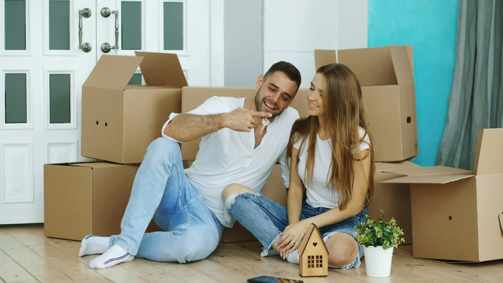 Casal sentado entre caixas de mudança, com a chave da casa nova na mão