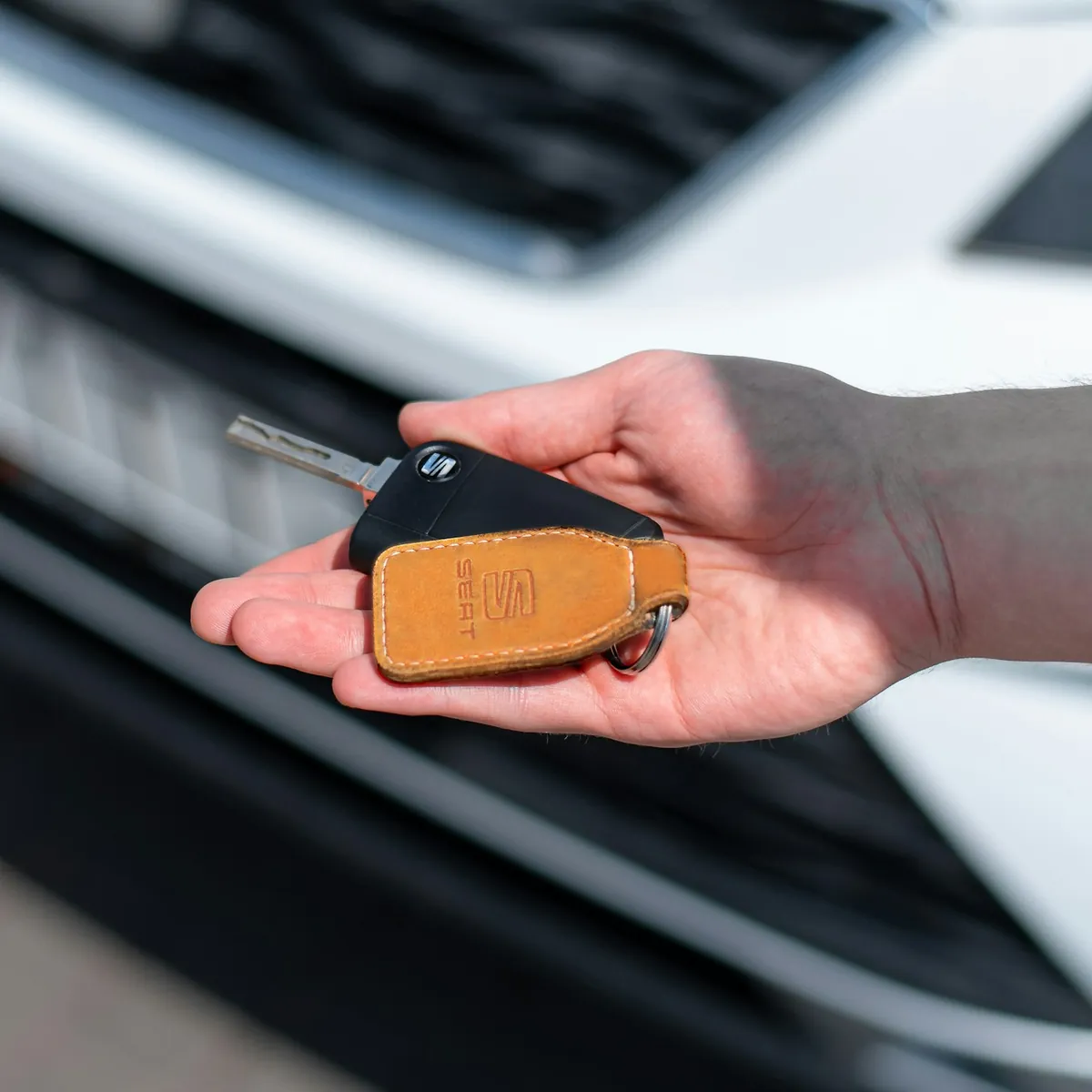 Mão segurando a chave de um carro, com o carro ao fundo